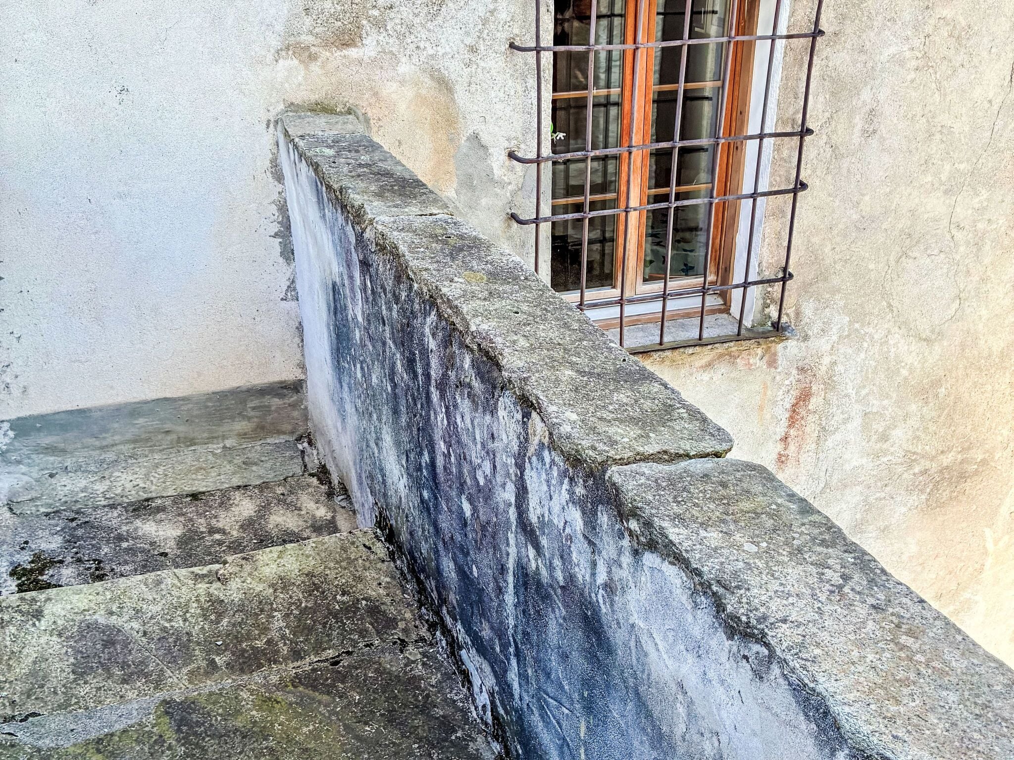 Eine Betonstairtreppe mit Metallgeländer, die zu einem Fenster mit Holzgitter führt.