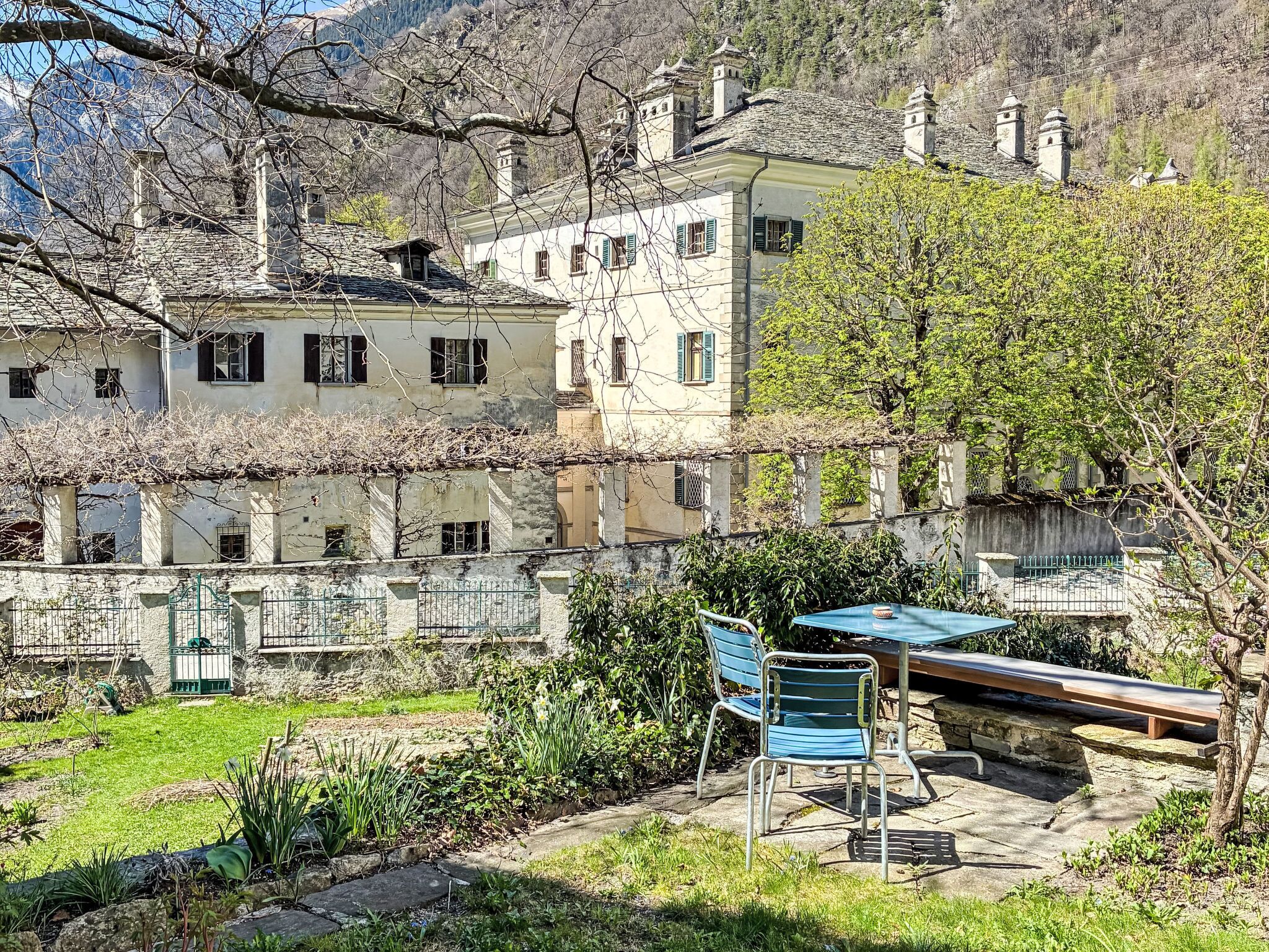 Ein Innenhof mit Tisch und Stühlen, umgeben von Gebäuden mit Steinmauern und einem Blick auf das Gebirge.