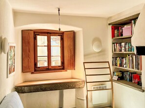 A room with a built-in bench, a bookshelf, and a window with wooden shutters.