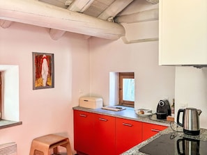A kitchen with red cabinets, a countertop, a coffee maker, and a window. - Casa Rederer by Interhome (Bondo)