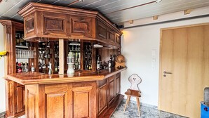 Eine Bar mit Holzsäulen, einem kleinen Hocker und verschiedenen Flaschen und Gläsern.