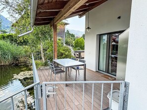 A wooden deck with a table and chairs, overlooking a body of water and greenery. - Köbihaus am Sagibach by Interhome (Alpnach)