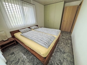 Un dormitorio con cama, armario y ventana con cortinas.