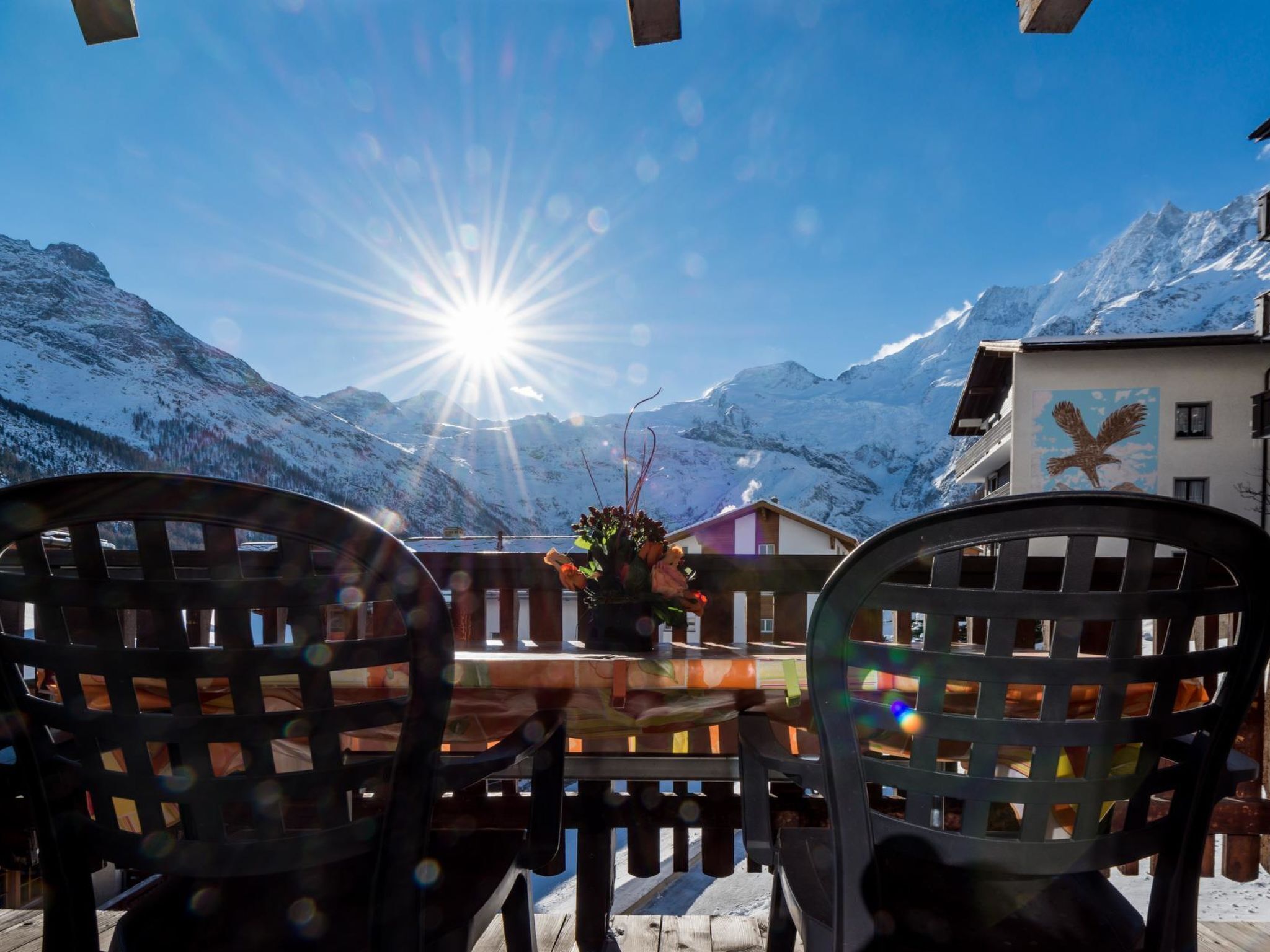 Une table avec des chaises, une vue sur la montagne et un bâtiment orné d’une fresque représentant un aigle.