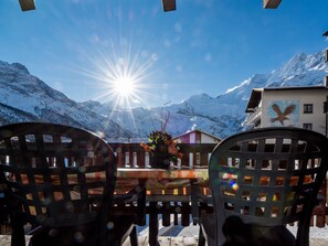 A table with chairs, a mountain view, and a building with an eagle mural. - Chalet Bambi by Interhome (Saas-Fee)