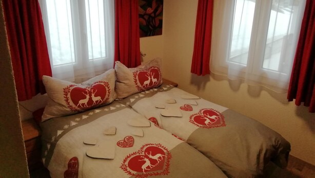 Een slaapkamer met een bed, rode gordijnen en een schilderij aan de muur.