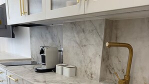 Eine Küche mit weißen Schränken, goldenen Griffen, einer Marmorarbeitsplatte, einer Spüle und einer Kaffeemaschine.