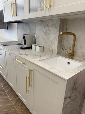 Eine Küche mit weißen Schränken, goldenen Griffen, einer Marmorarbeitsplatte, einer Spüle und einer Kaffeemaschine.