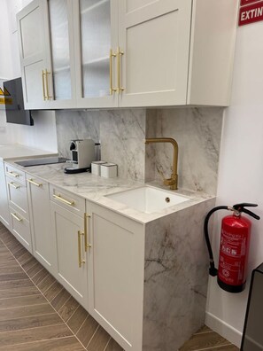 A kitchen with white cabinets, a marble countertop, a gold faucet, and a red fire extinguisher. - La Casona de les Arts 3 - Oceanográfic (València)