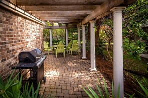 En overdækket terrasse med røde mursten, en grill og grønne stole.
