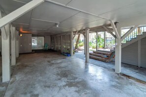 A spacious covered area with a concrete floor, a staircase leading to an upper level, and a door leading to an adjacent room. - 4BR Beach House w/ Covered Porches, Game Room & Shared Creek Dock Access (Pawleys Island)