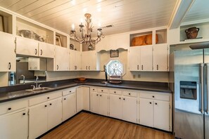 Una cocina con armarios blancos, un refrigerador de acero inoxidable, una lámpara de araña y piso de madera.