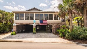 A two-story building with a garage entrance, American flag, and 'NO PARKING' signs. - 4BR Beach House w/ Covered Porches, Game Room & Shared Creek Dock Access (Pawleys Island)