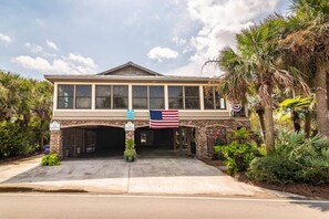 A two-story building with a garage entrance, American flag, and 'NO PARKING' signs. - 4BR Beach House w/ Covered Porches, Game Room & Shared Creek Dock Access (Pawleys Island)