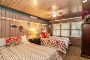 A bedroom with two beds, wooden walls, a ceiling fan, and a window with blinds. - Spacious Coastal Home Near Beach | Gourmet Kitchen, Game Room & Fishing Dock (Pawleys Island)