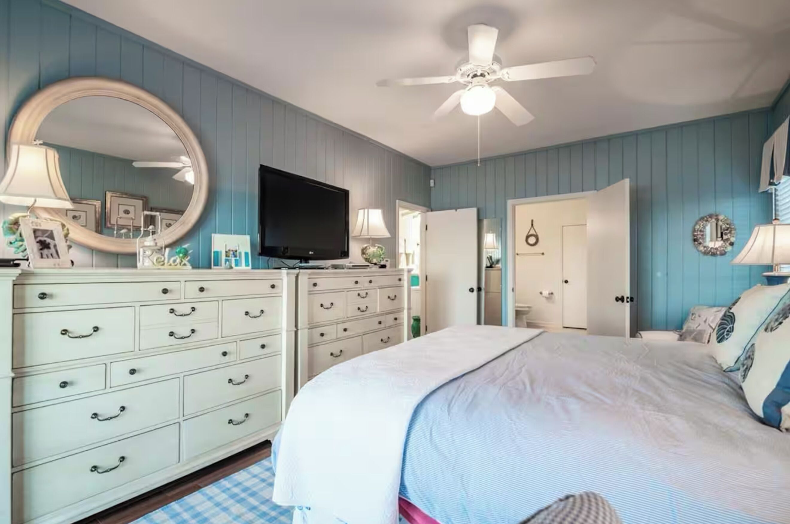 A bedroom with a bed, dresser, television, and a ceiling fan.