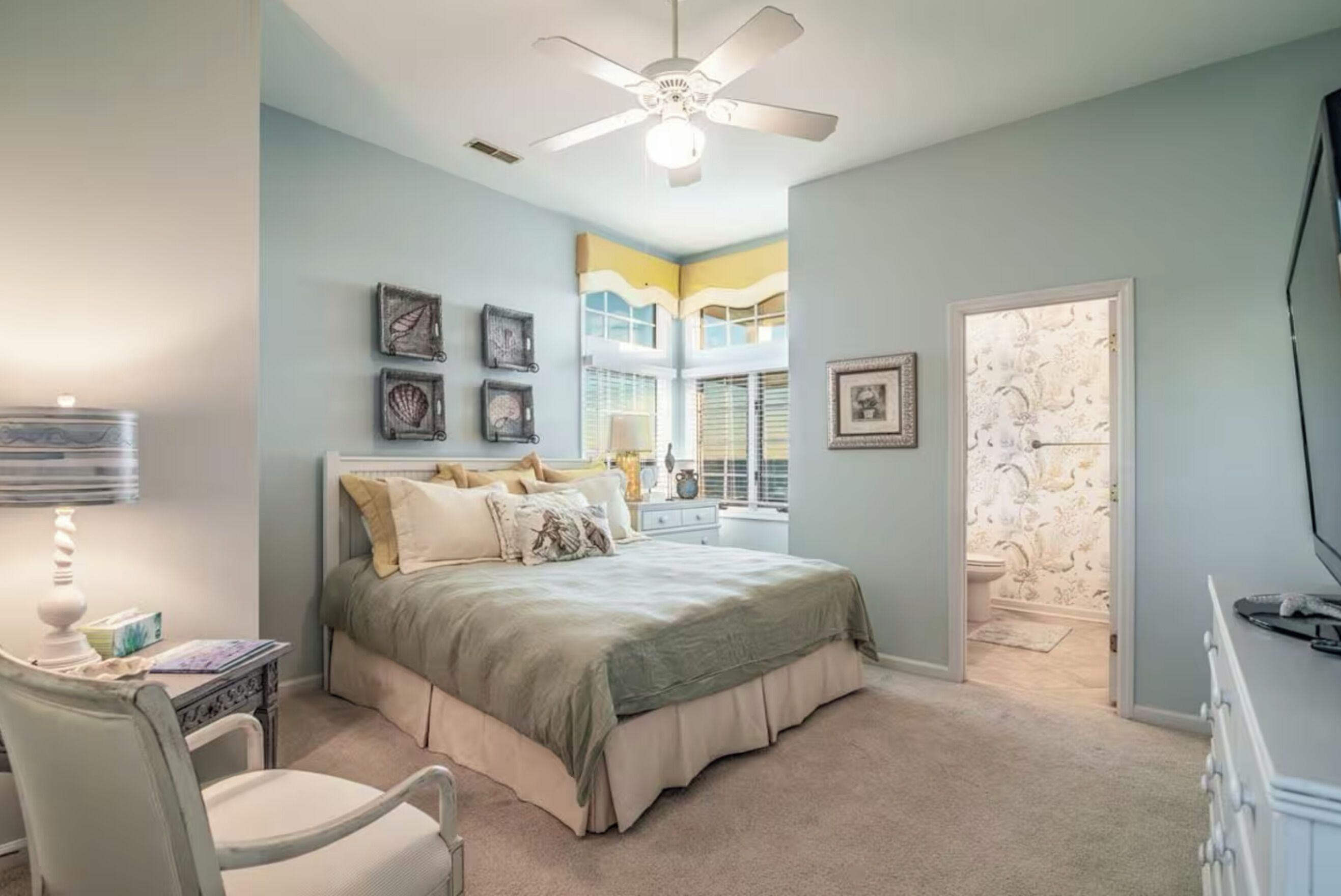 A bedroom with a bed, a chair, a ceiling fan, and a window with blinds.