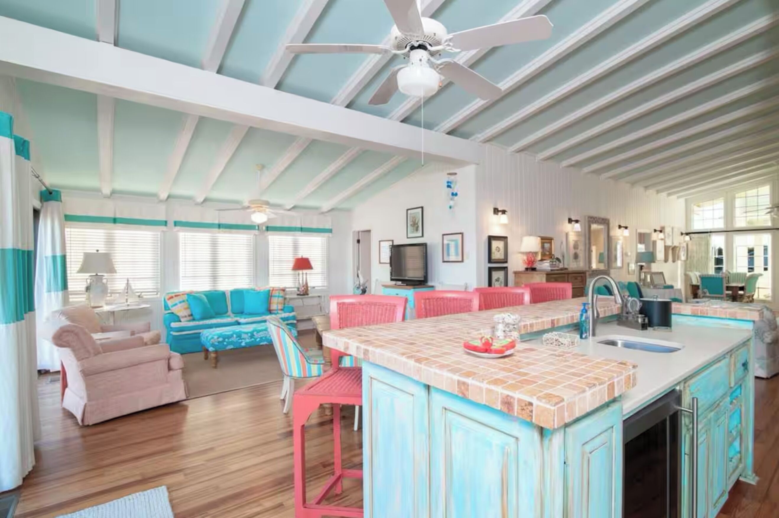 A spacious living area with a large island, a kitchen with a sink, and a dining area with red chairs.