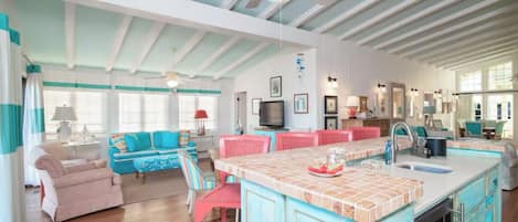 A spacious living area with a large island, a kitchen with a sink, and a dining area with red chairs.