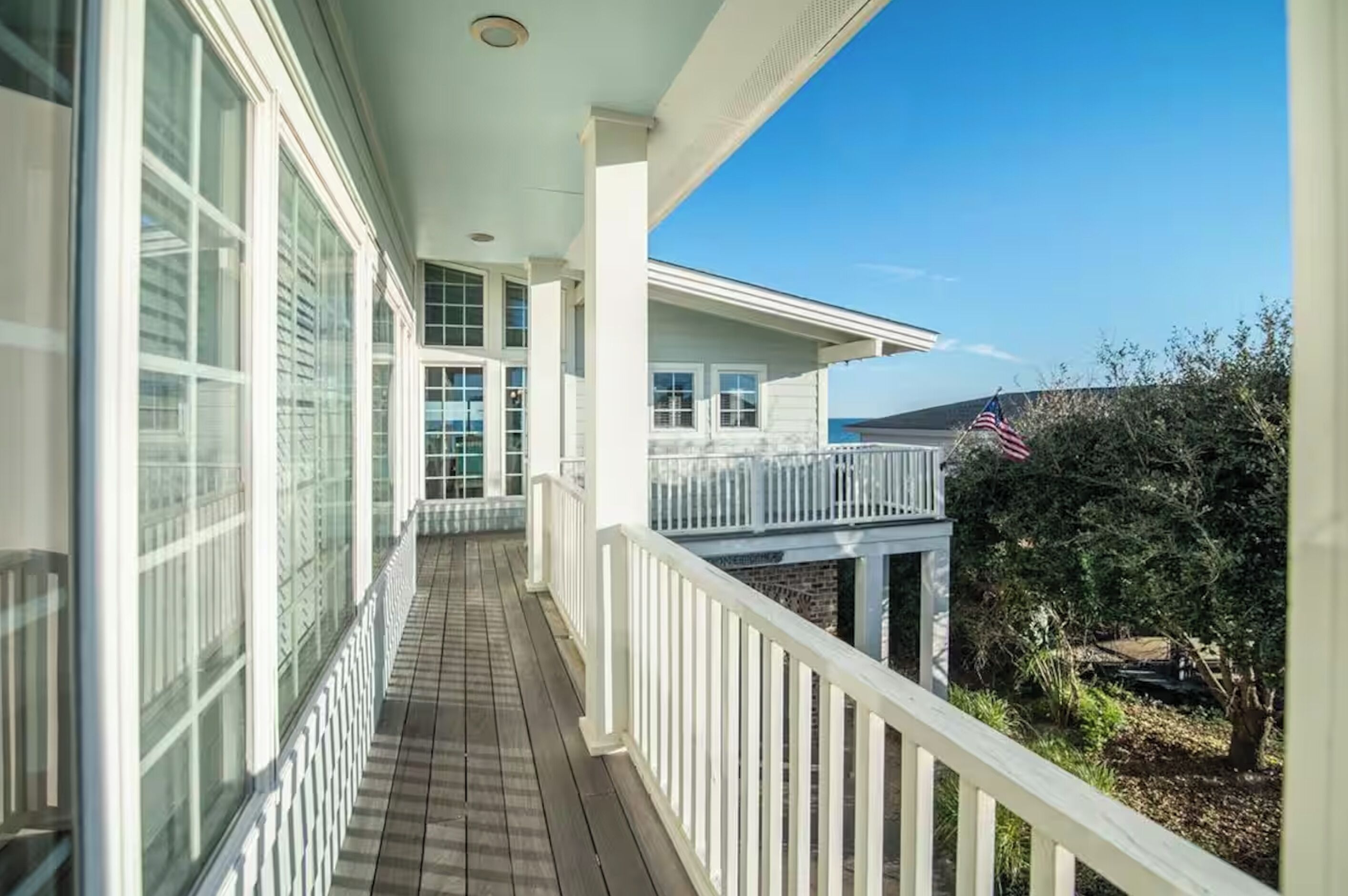 A covered balcony with a view of the ocean, white railings, and a small American flag.