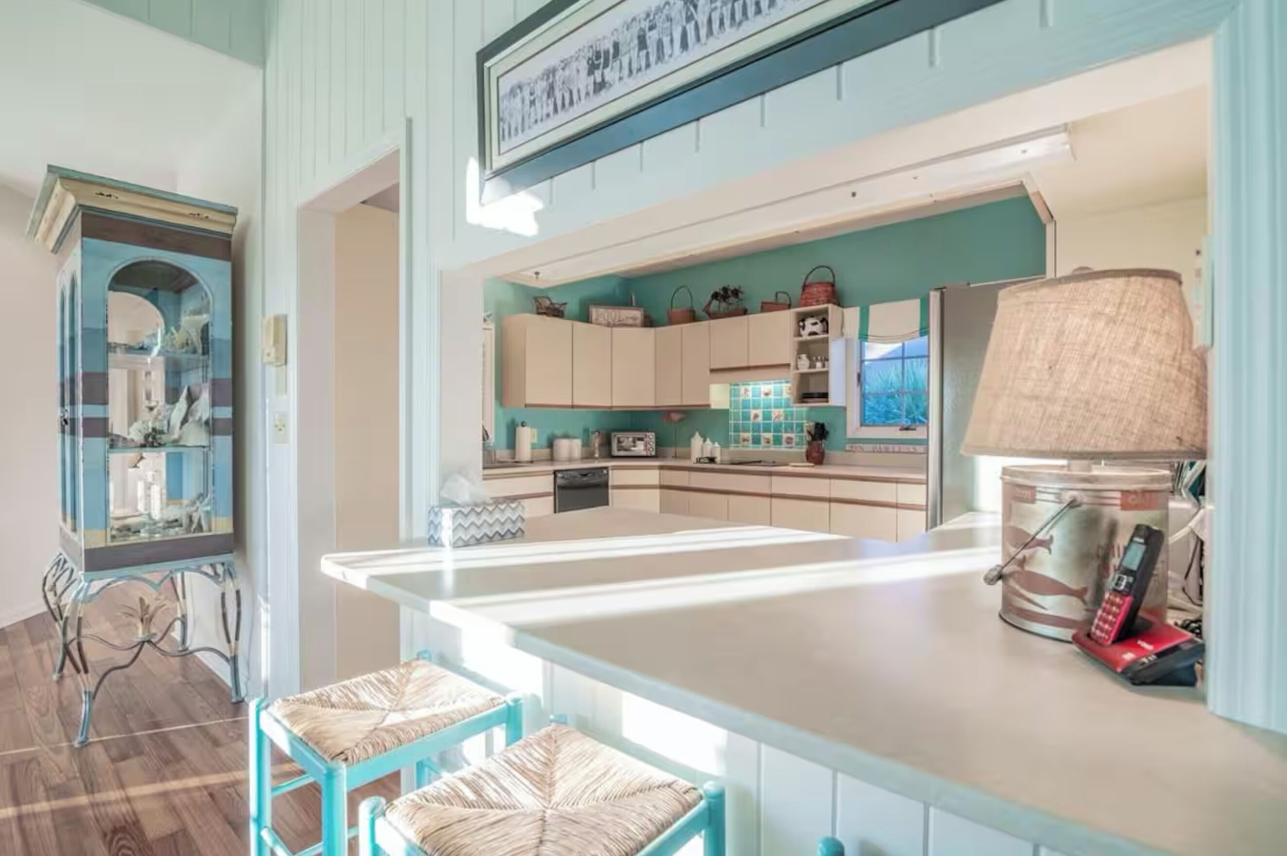 A modern kitchen with a central island, light-colored cabinets, and a teal backsplash.