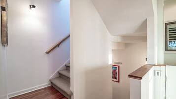 A staircase with a wooden handrail leading to a landing, a small kitchen area with a refrigerator, and a wall-mounted light fixture.