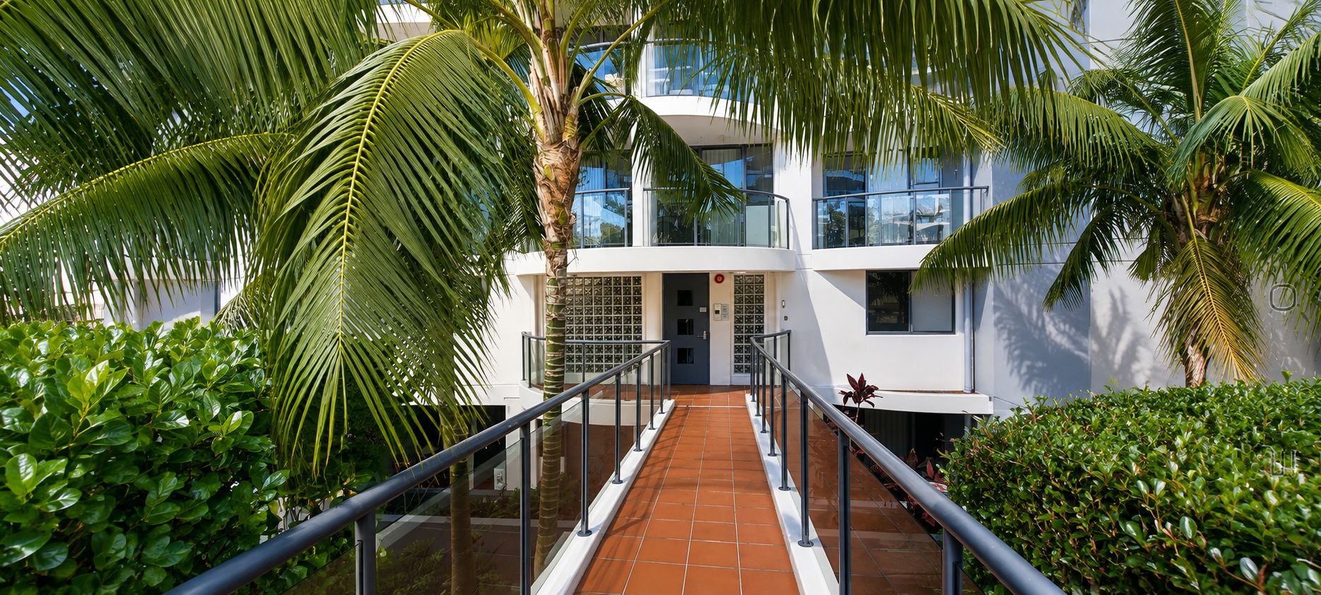 A modern building with a glass facade, a covered walkway, and lush greenery.