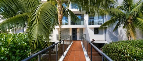 A modern building with a glass facade, a covered walkway, and lush greenery.