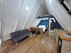 A loft-style room with a sofa, a small round table, and a kitchenette area. - Ecos del Manantial (Villarrica)