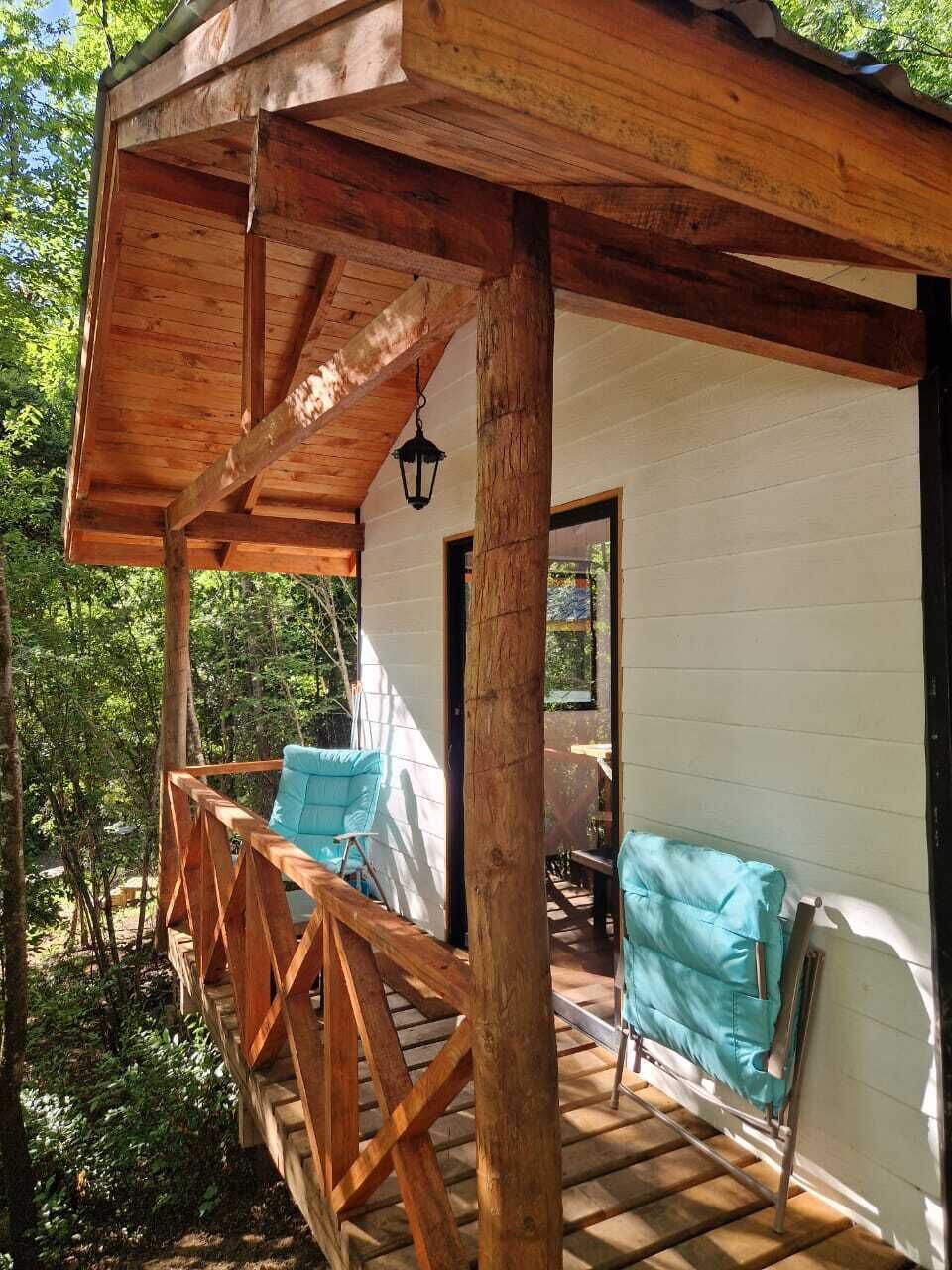 A wooden deck with a covered seating area, a door, and a view of the surrounding greenery.