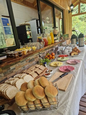 A buffet with various food items and beverages, including bread, pastries, fruits, and a coffee station. - Ecos del Manantial (Villarrica)