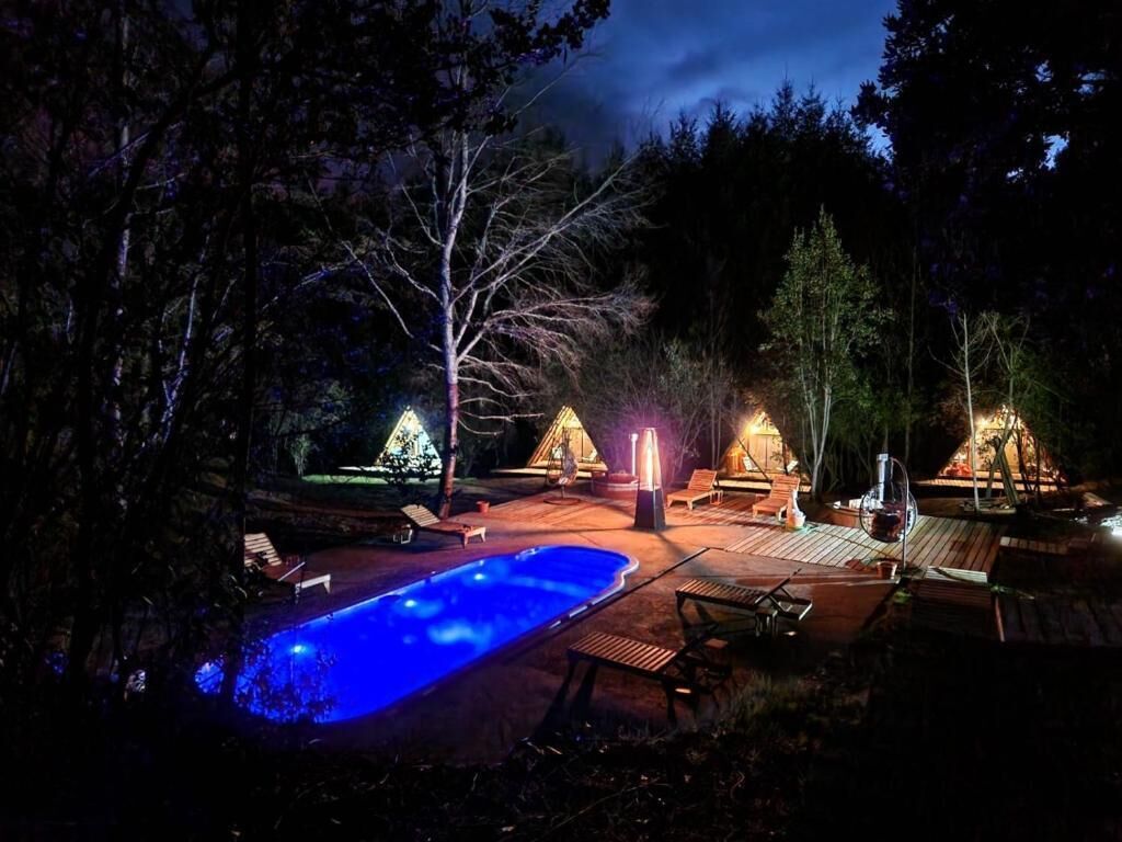A nighttime outdoor area with a swimming pool, lounge chairs, and a fire pit.