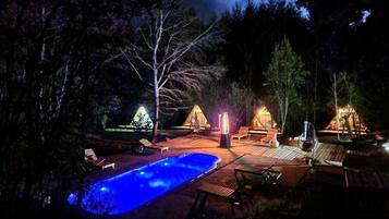 Espaço ao ar livre à noite, com piscina, espreguiçadeiras e uma lareira.