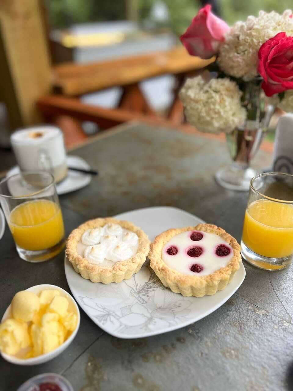 Une table mise pour le petit-déjeuner avec deux scones, un bol de beurre et deux verres de jus d’orange.