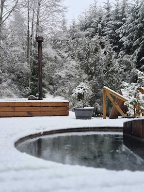 A snow-covered outdoor area with a wooden deck, a metal structure, and a small pond.