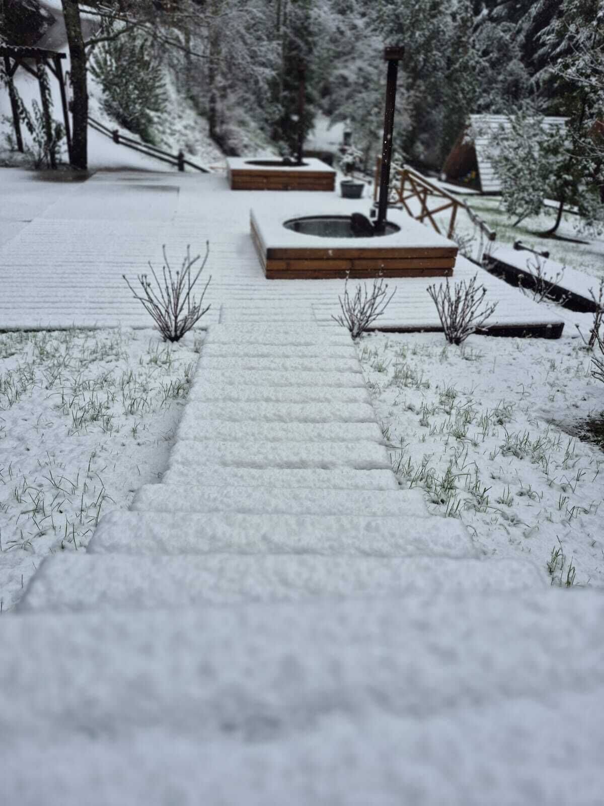 A snow-covered pathway leading to a wooden deck area with a fire pit.