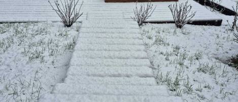 A snow-covered pathway leading to a wooden deck area with a fire pit.