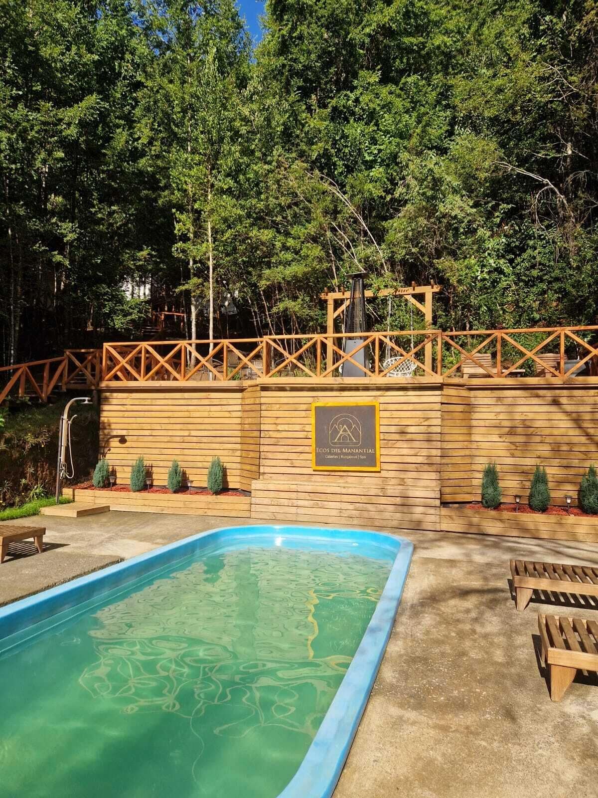 A wooden deck with a pool, surrounded by trees and a wooden wall with a plaque.
