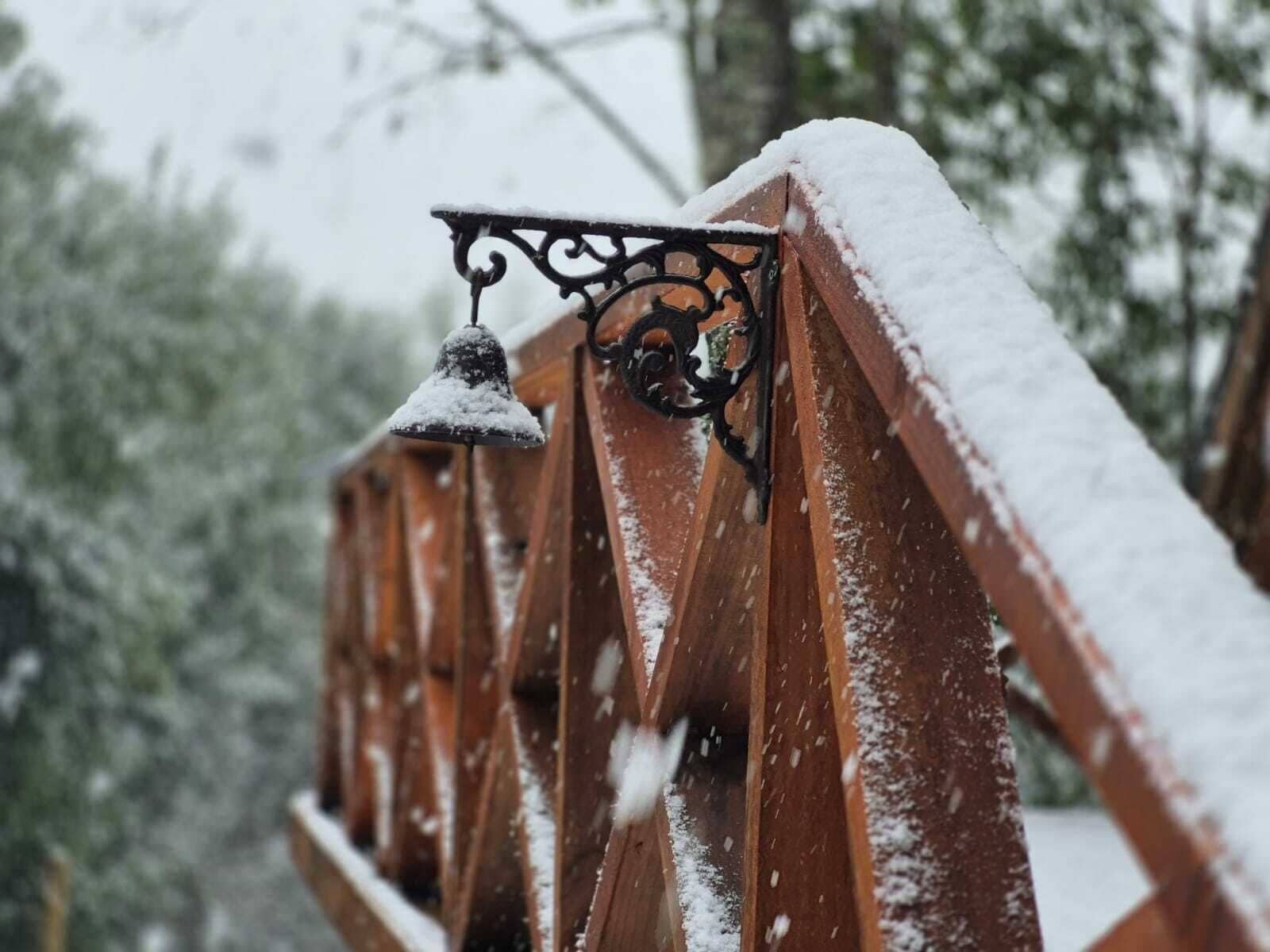 Une rambarde métallique, dont la main courante est recouverte de neige, et une cloche.