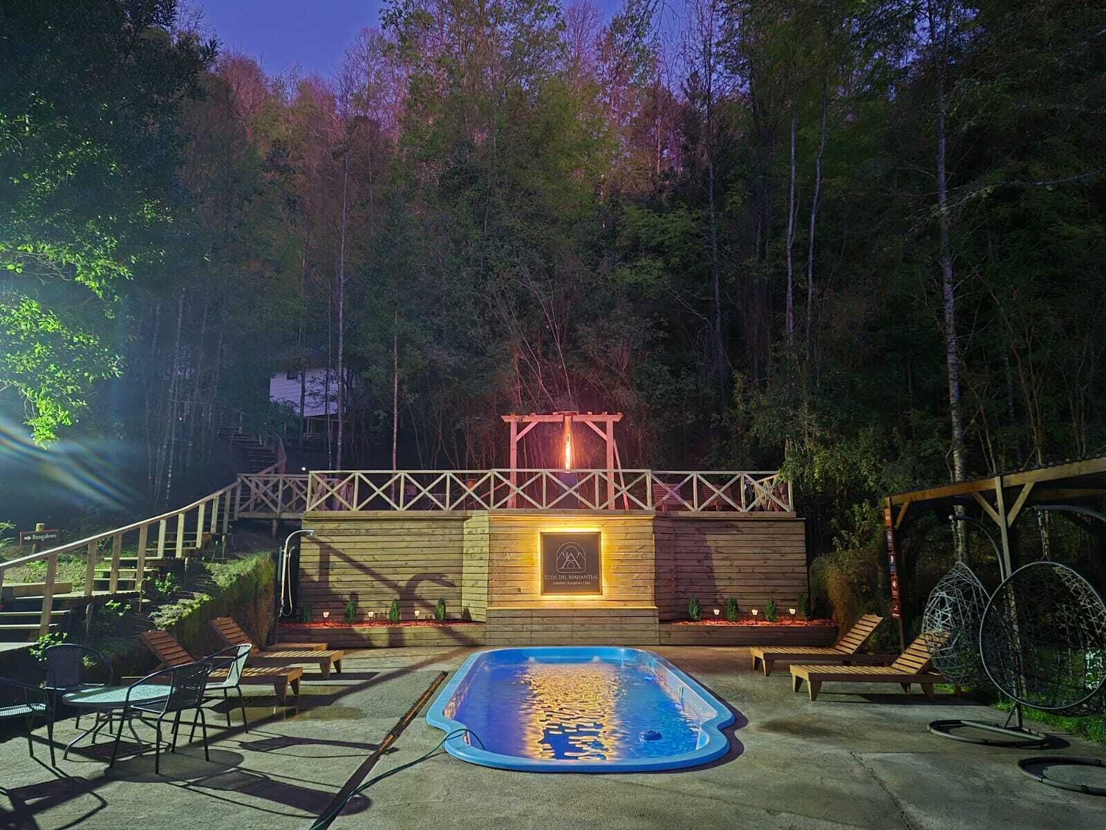 An outdoor swimming pool area with a wooden deck, lounge chairs, and a pergola structure.