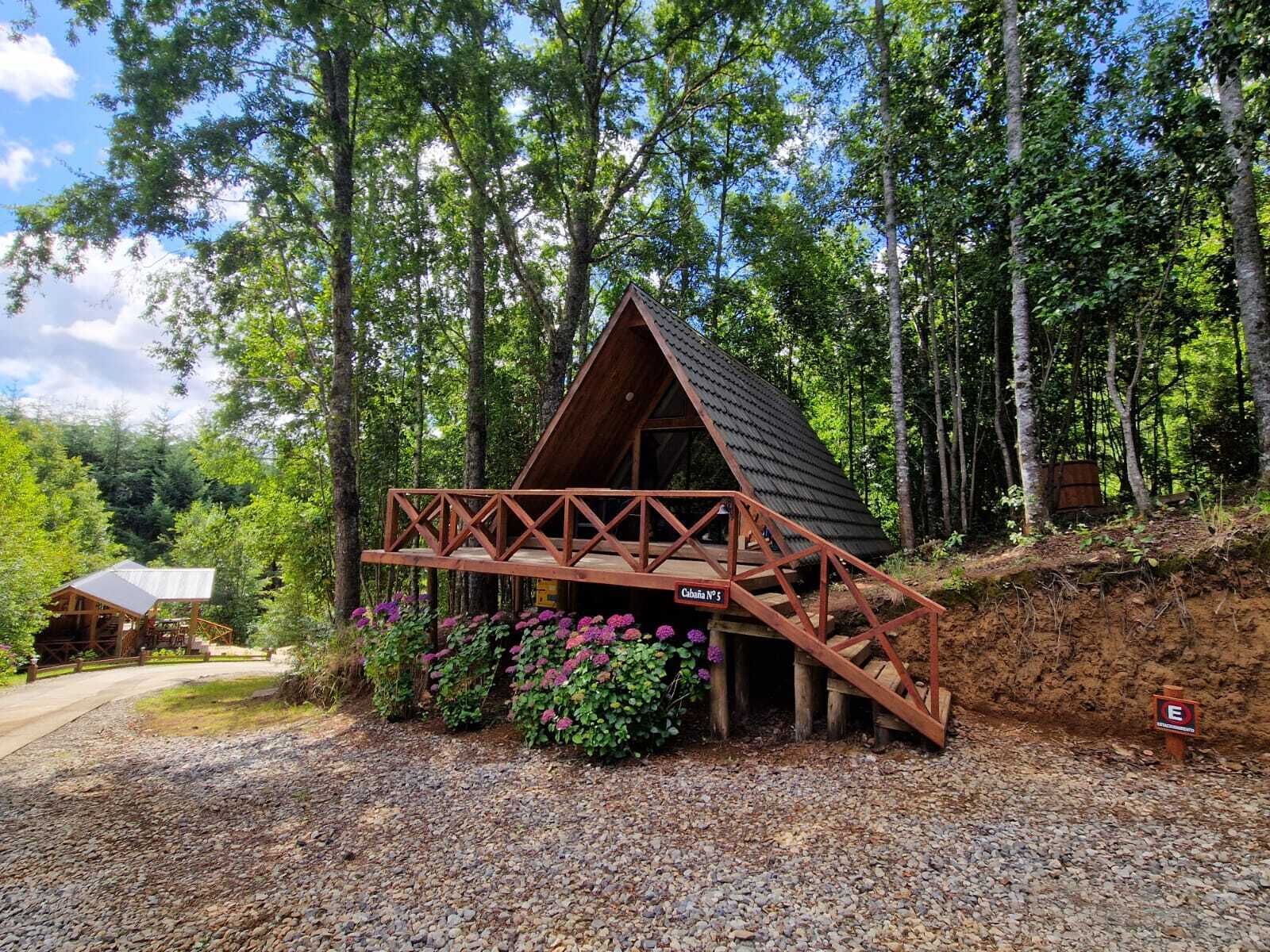Uma cabana de madeira com telhado inclinado, um deck de madeira e um caminho de cascalho que a leva até ela.
