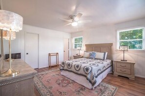 Une chambre à coucher avec un lit, des tables de chevet, un ventilateur de plafond et une fenêtre avec des stores.