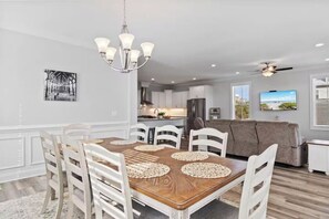 A dining area with a wooden table, white chairs, and a chandelier. - Panoramic Ocean View Retreat Near South Litchfield Beach w/ Resort Access (Pawleys Island)