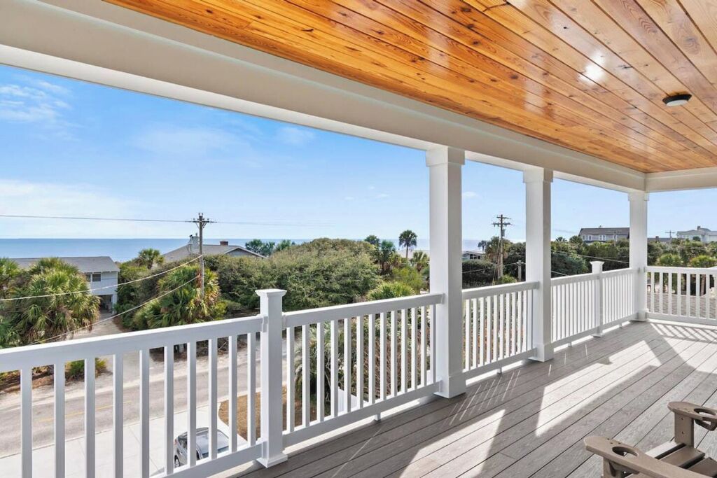 A covered porch with a view of the ocean and surrounding greenery.