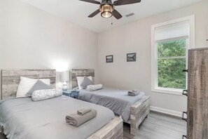 A bedroom with two beds, a ceiling fan, a window with a view of greenery, and a wooden wardrobe. - Family-Friendly Coastal Retreat Near the Beach w/ Pools, Golf & Bike Trails (Pawleys Island)