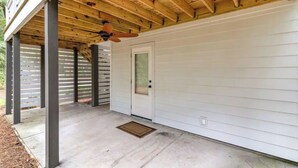 Un porche cubierto con ventilador de techo, una puerta con ventana y piso de concreto.