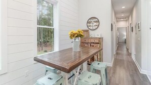 Un comedor con una mesa de madera y taburetes azul claro, un jarrón con flores amarillas y un reloj en la pared.