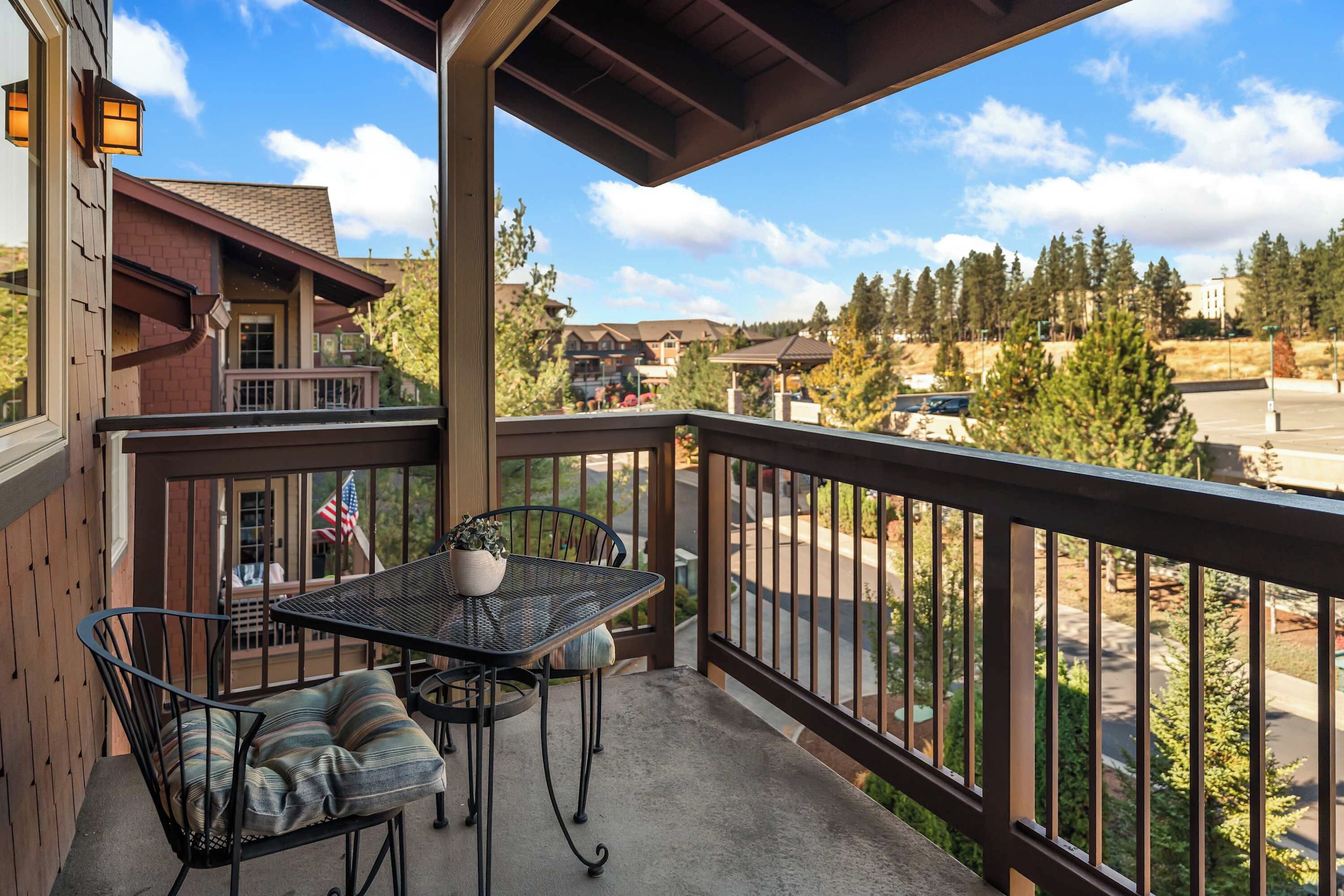 A balcony with a table and chairs, overlooking a residential area with houses and trees.