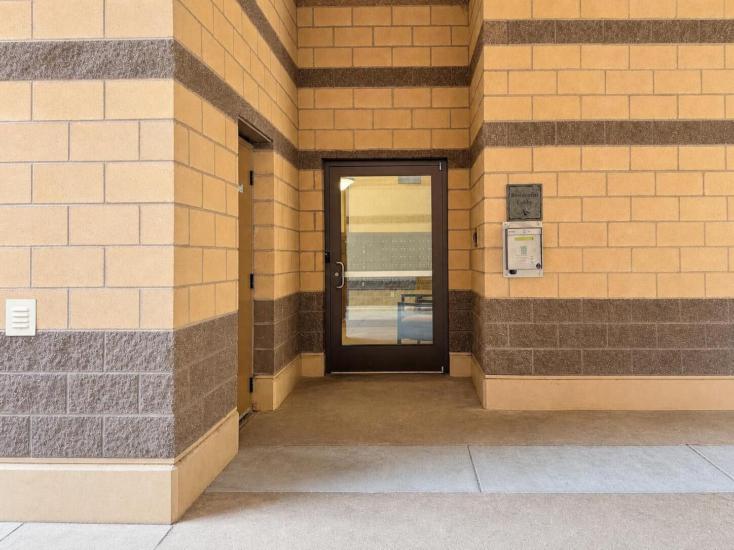 A building entrance with a glass door, a sign indicating a residential lobby, and a security intercom system.