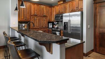 A kitchen with wooden cabinets, a stainless steel refrigerator, a microwave, a coffee maker, and a granite countertop.